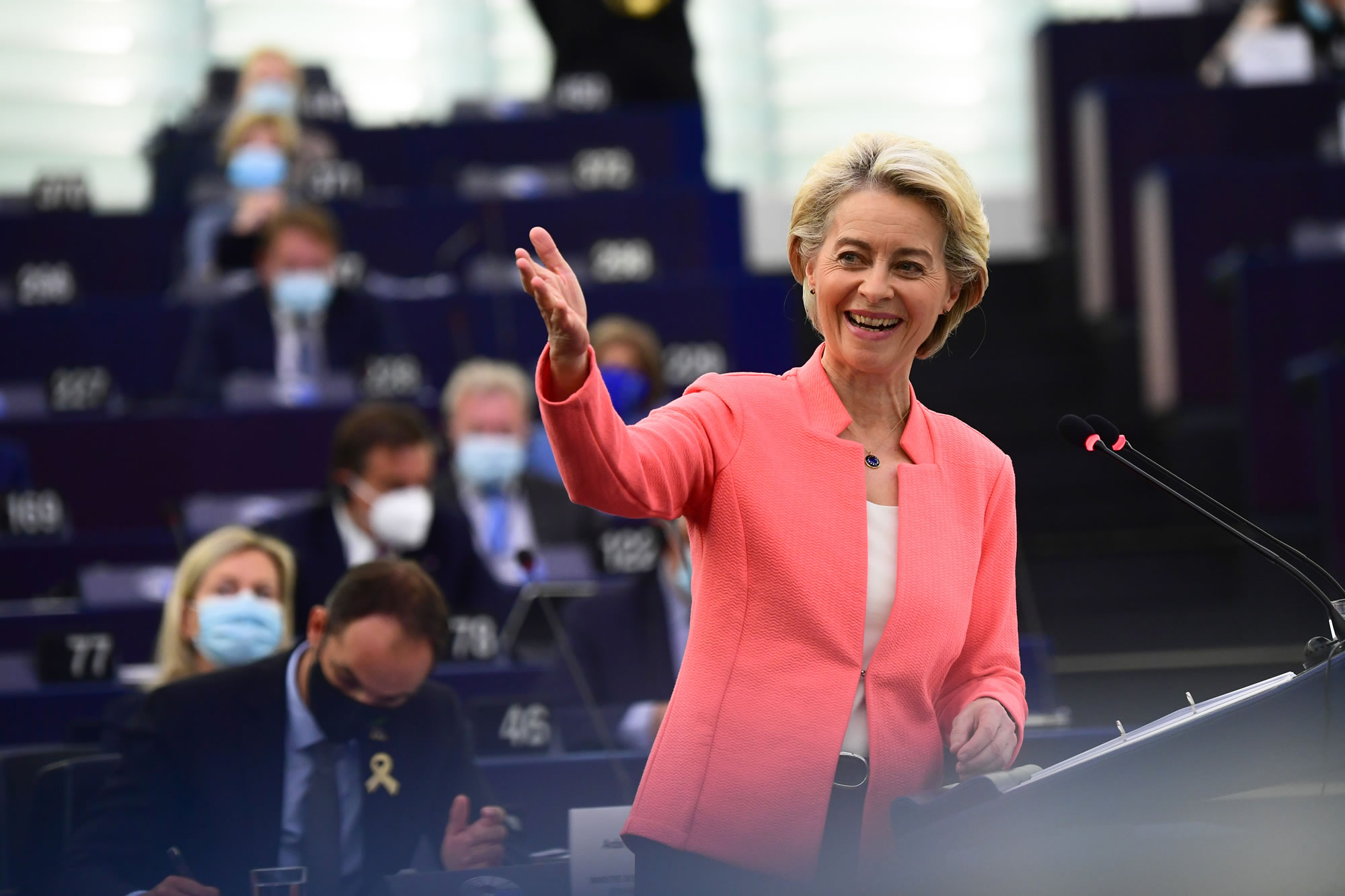 Ursula von der Leyen z nasmehom stoji na odru in z dvignjeno roko gestikulira občinstvu.