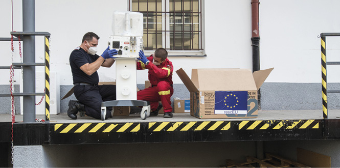 Dwóch mężczyzn montuje wyrób medyczny na doku załadunkowym. Z boku pudło z flagą europejską.