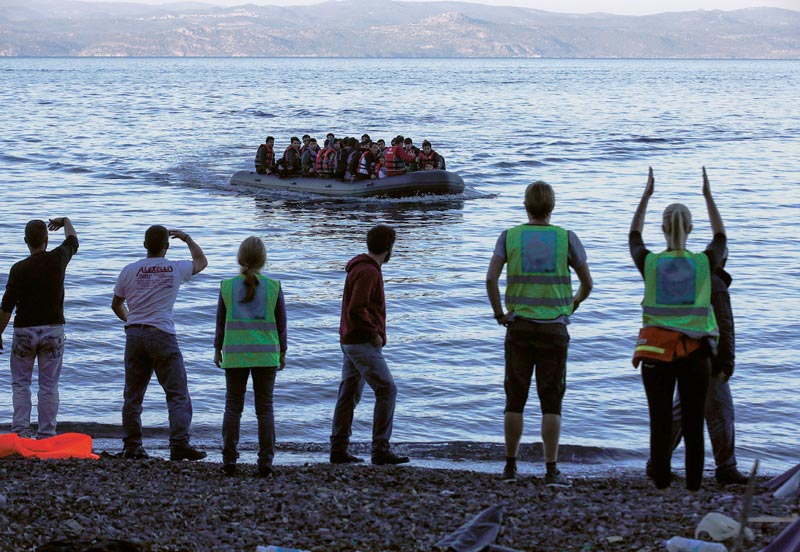 Refugiados em embarcação abordam praia de ilha grega.