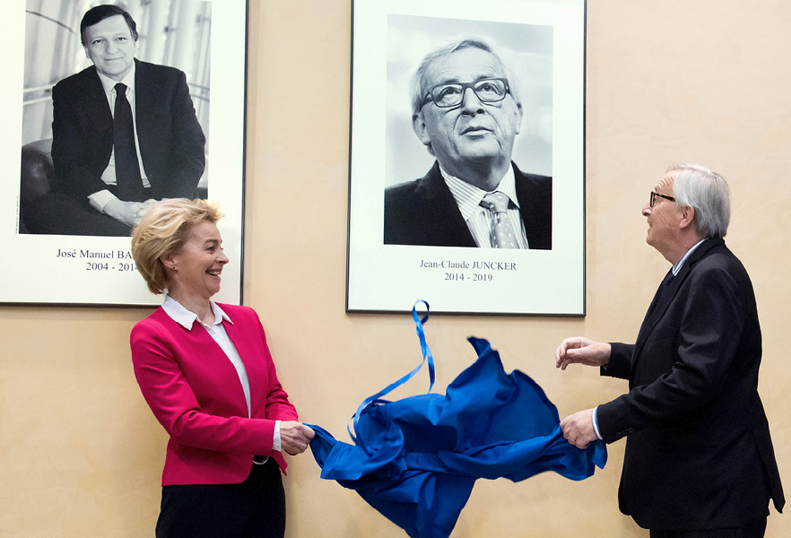 Ursula von der Leyen agus Jean-Claude Juncker, aoibh an gháire ar an mbeirt acu agus iad ag nochtadh phortráid Juncker le chéile