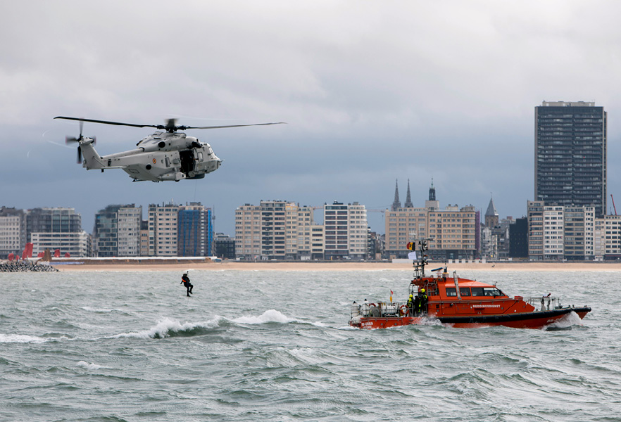 Hélicoptère retirant un secouriste de l’eau derrière un navire des gardes-côtes.