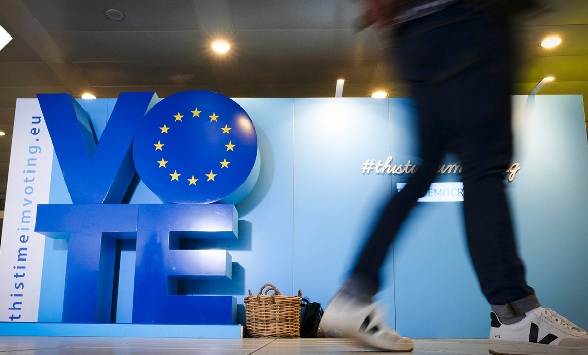 Chodec prochází okolo instalace z písmen s nápisem „VOTE“ a vlajky Evropské unie