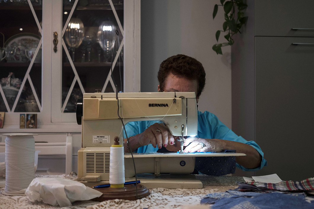 A foto mostra uma voluntária a trabalhar numa máquina de costura em sua casa.