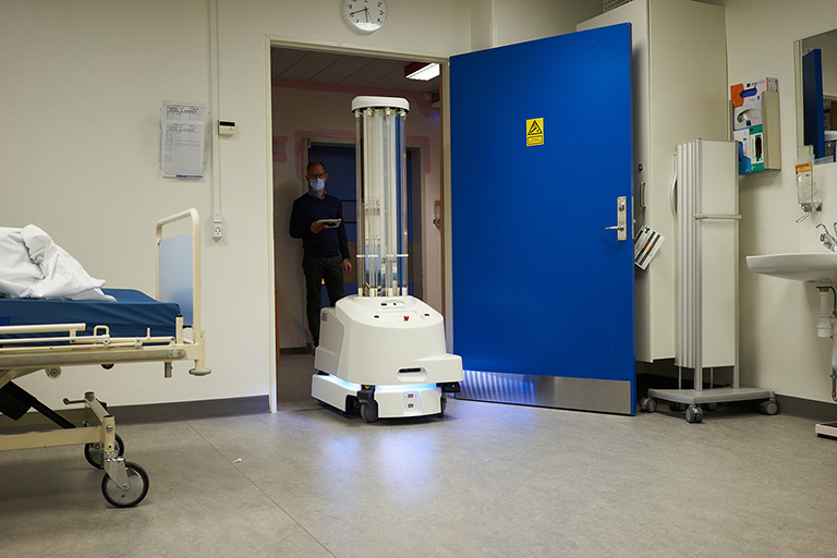 Uma máquina telecomandada entra num quarto de hospital, vislumbrando-se por trás o profissional de saúde que a controla.